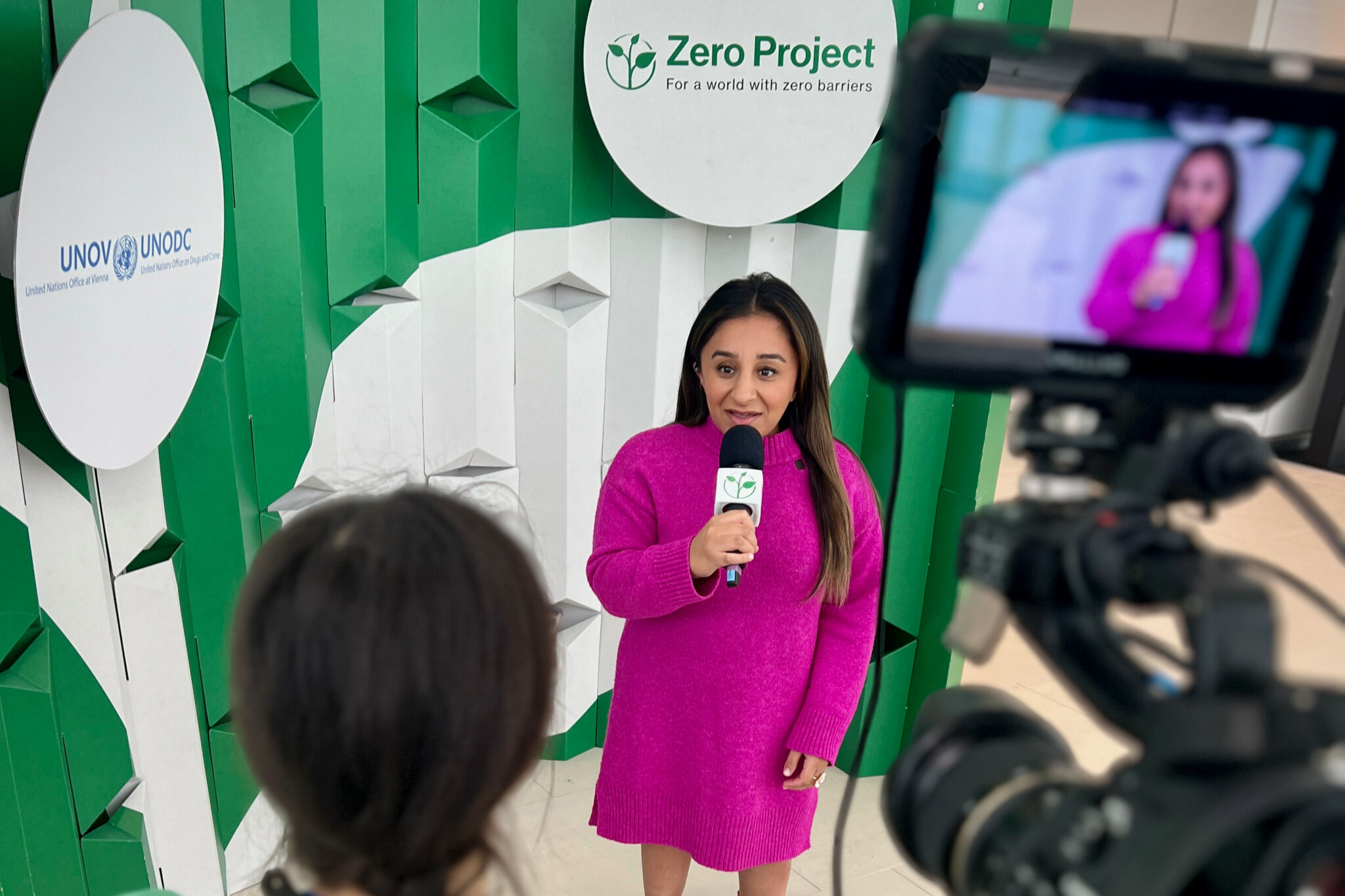 Die britische Behindertenaktivistin Shani Dhanda (kleinwüchsige Frau mit pinkem Kleid) gibt eine Interview bei der Zero Project Konferenz