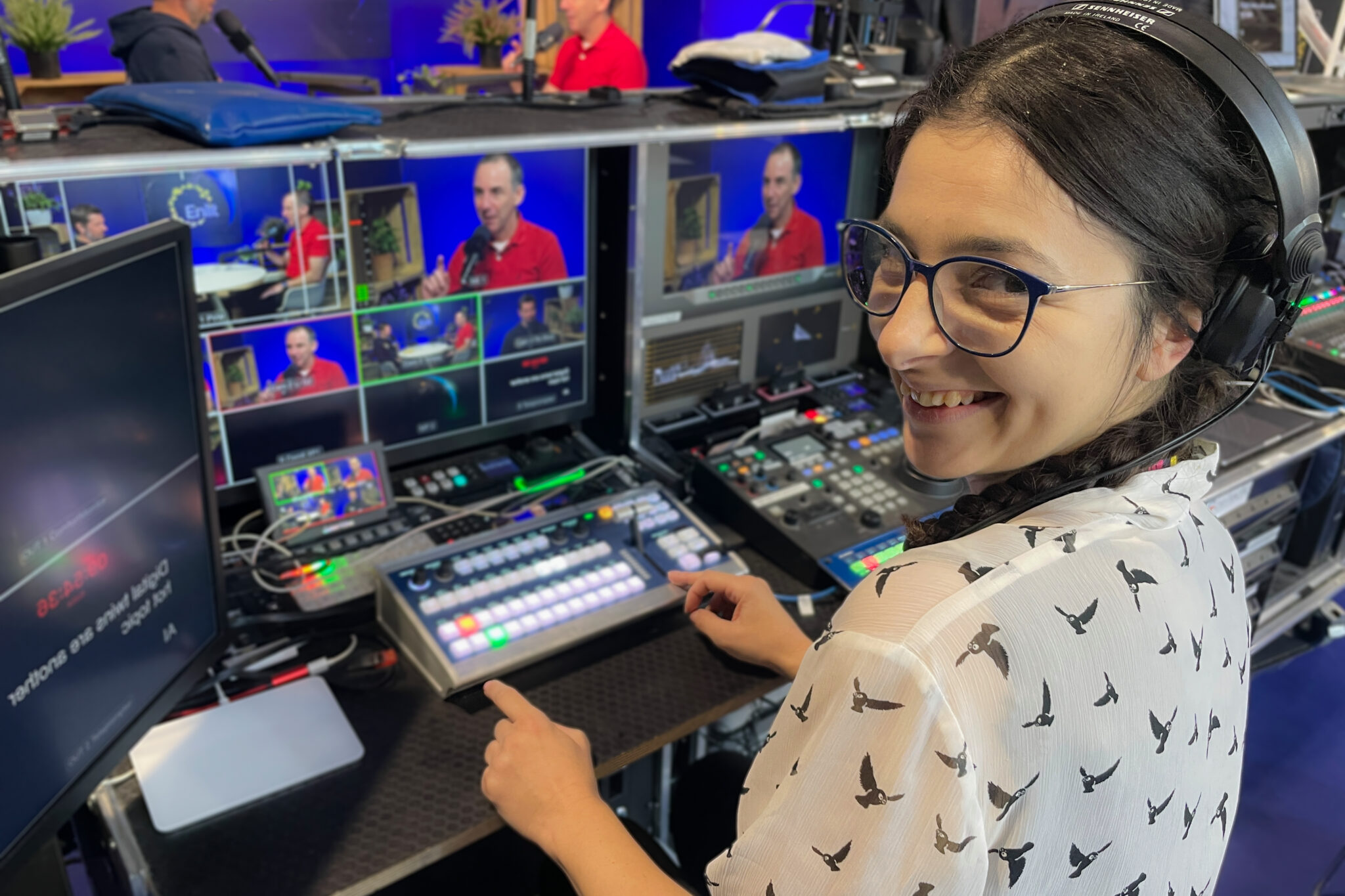 Mobiles Regiestudio mit vielen Monitoren. Antina (Frau mit dunklen Haaren und weißem Shirt) drückt auf den Knöpfen, blickt zu Kamera und Lächelt. Mobiles Videostudio
